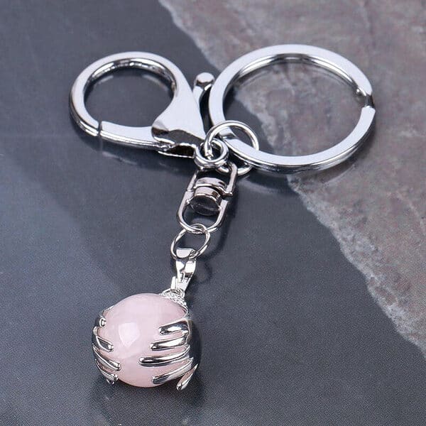 Porte-Clés Boule Porte-Bonheur avec un pendentif en forme de main entourant une boule en pierre naturelle de Quartz Rose vendu par la Boutique Z Comme Zen